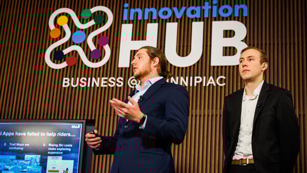 2 male students speaking in front of the Innovation Hub logo