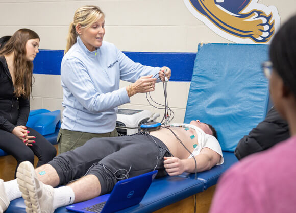 A faculty member and students conduct an EKG screening on a male student lying on a mat.