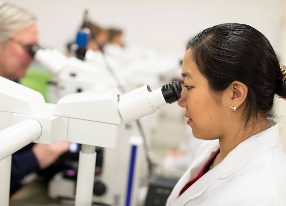 A student wearing a white coat looking into a microscope.