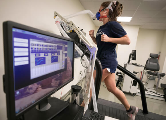 A female student running on a treadmill with a breathing mask collecting data shown on a computer