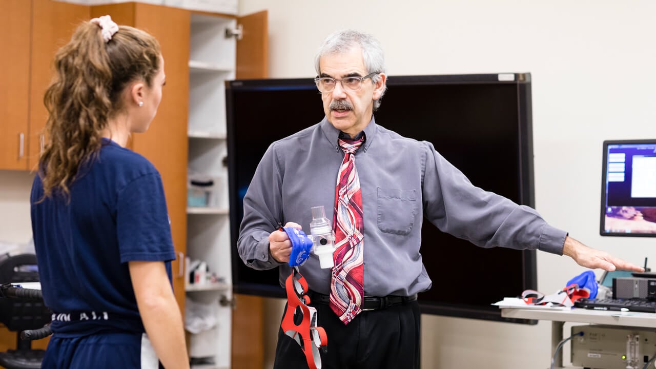 A student athlete receives direction from a professor for a stamina experiment in a biomechanics lab