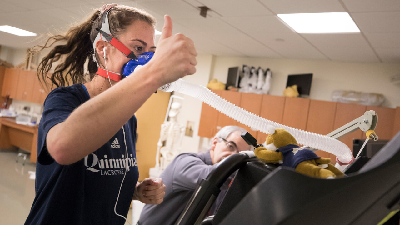 A student athlete gives a thumbs-up to her professor during a stamina experiment in a biomechanics lab