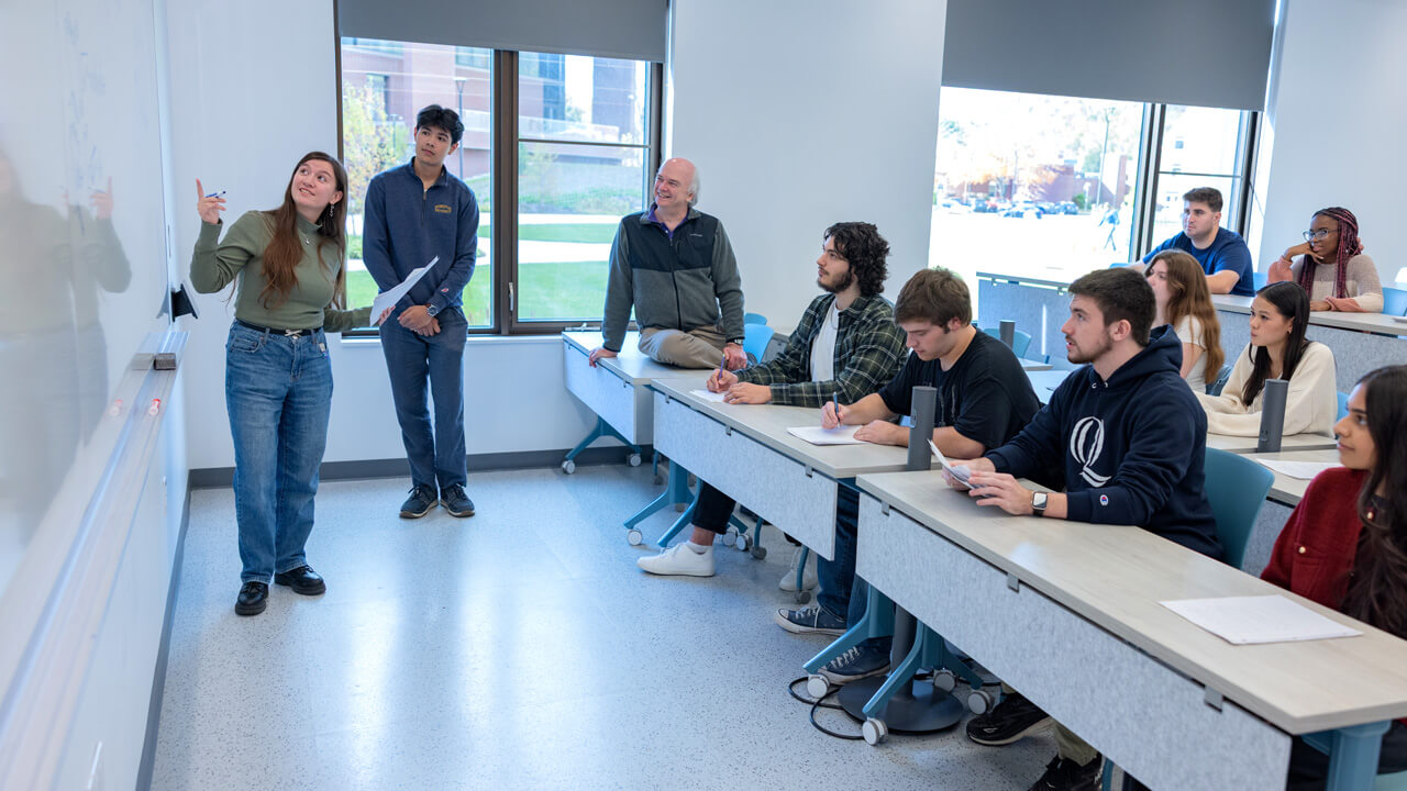 Two students presenting their work to their classmates and professor in the a classroom