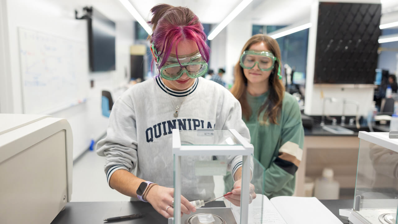 Pair of student wearing safety glasses as they conduct an experiment in a lab