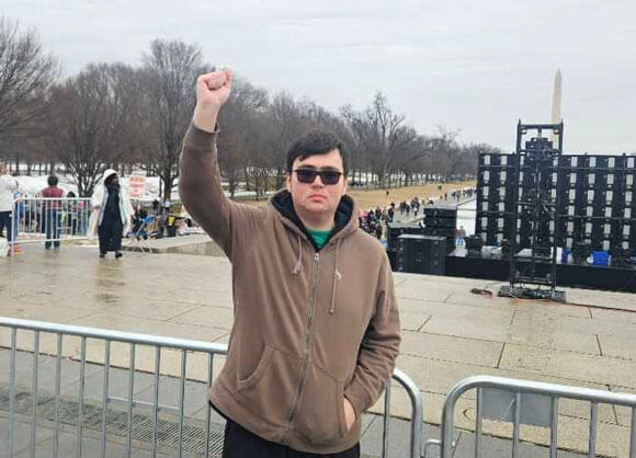 Student stands with their fist up with the Washington Monument in the distance.