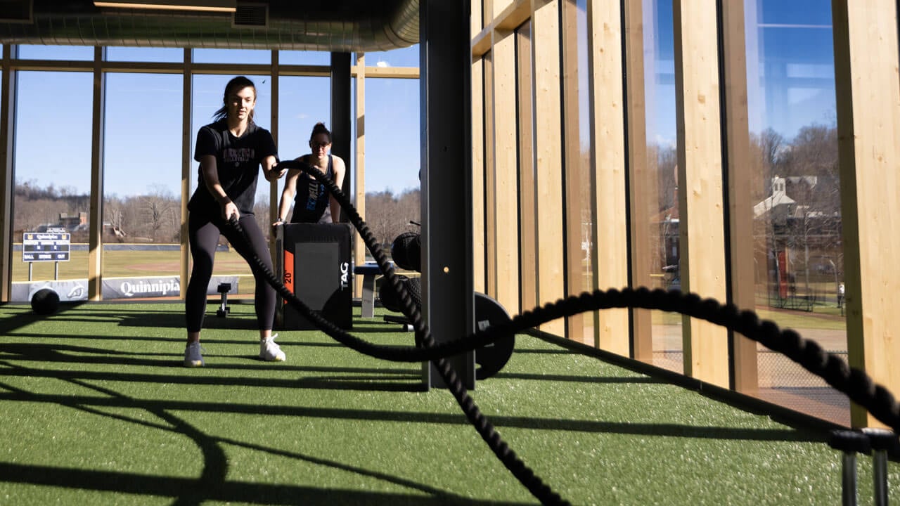 A student uses ropes to work out in RecWell on the turf.