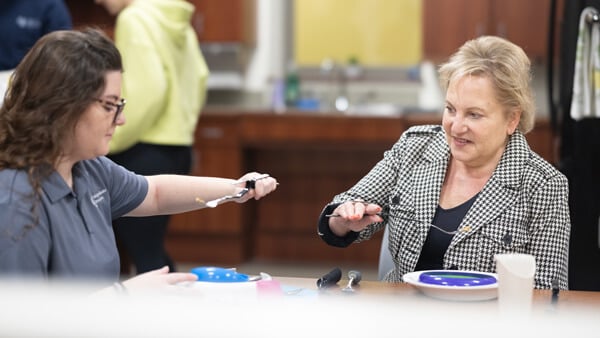 An OT professor instructs an OT student using a weighted spoon