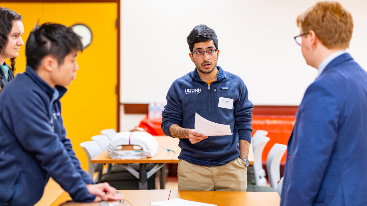 Three students watch and listen as another reads from a paper.