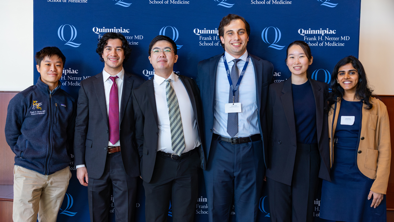 Six students pose for a photo in front of Quinnipiac backdrop.