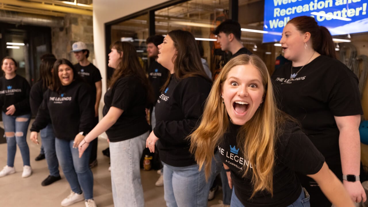 A student smiles enthusiastically next to her fellow singers in the acapella singing group the Legends