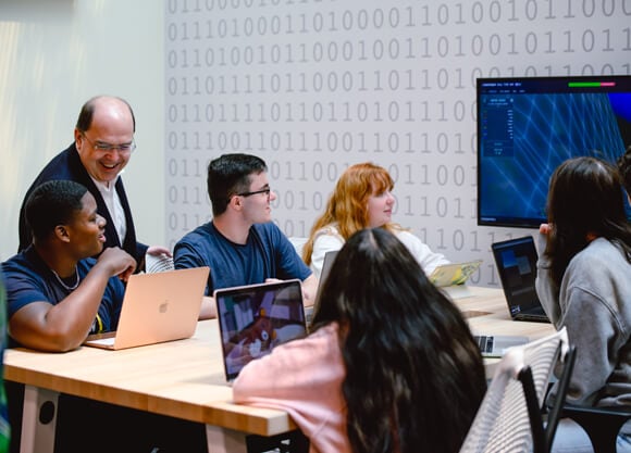 A professor interacting with students in a computing classroom