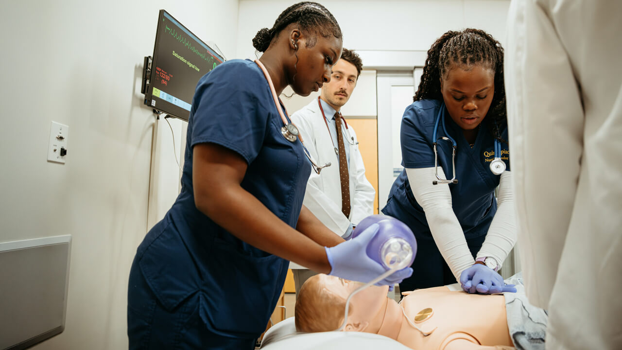 Nursing students perform chest compressions and administer breathing assistance to a patient during a simulation exercise.