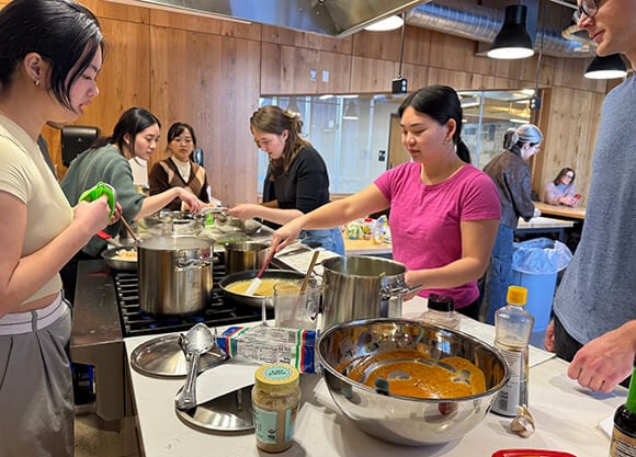 Group of students gathered around a kitchen island to cook pasta