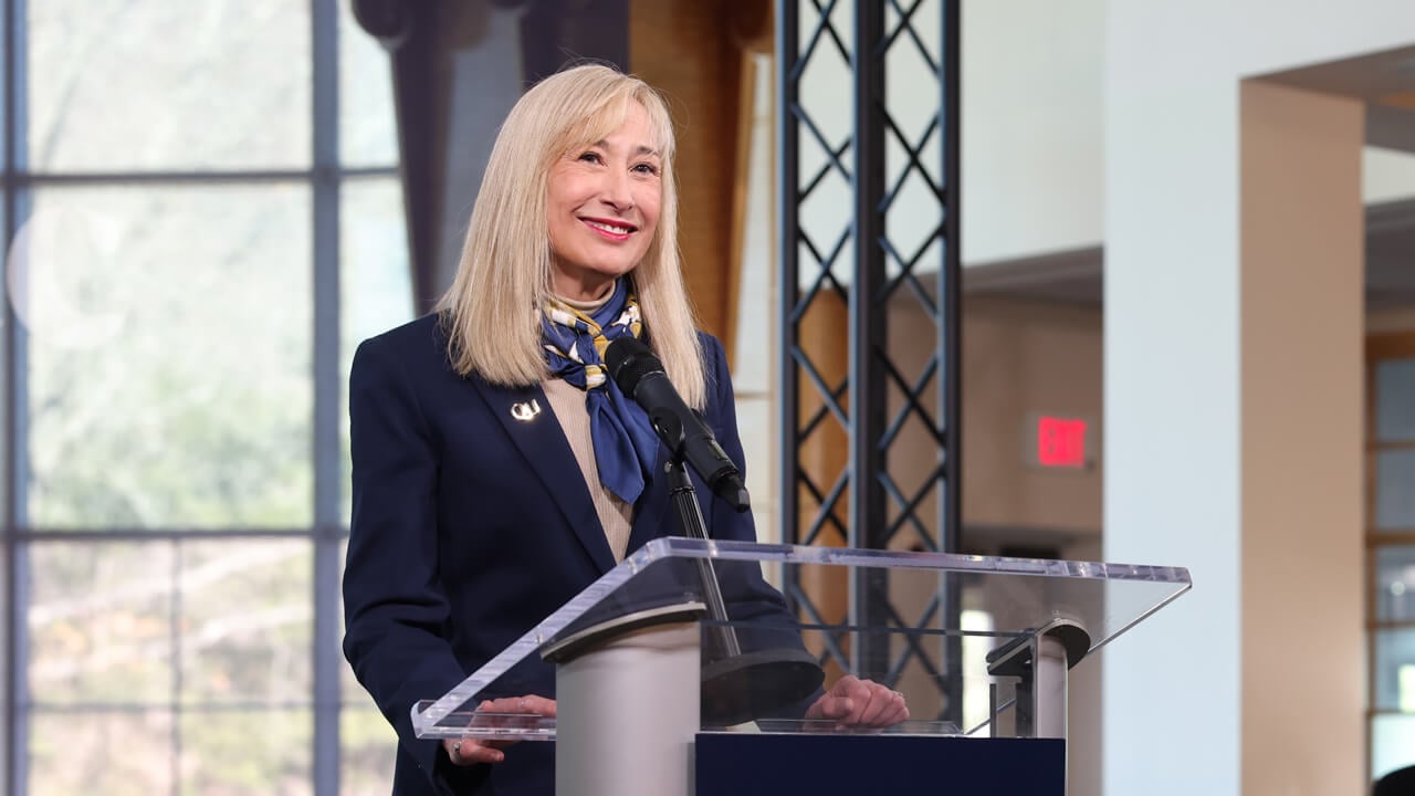 Marie Hardin smiles behind a podium in the open air studio