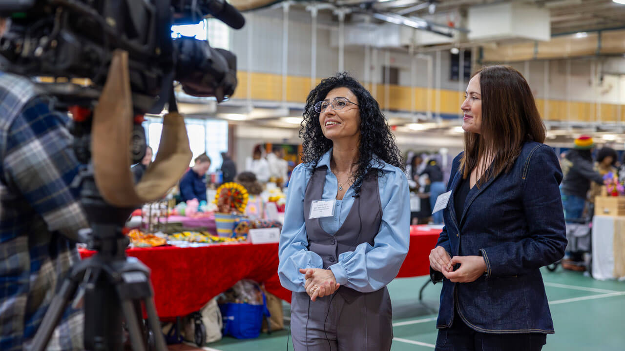 Two professors stand in front of a camera at the Sip and Shop.