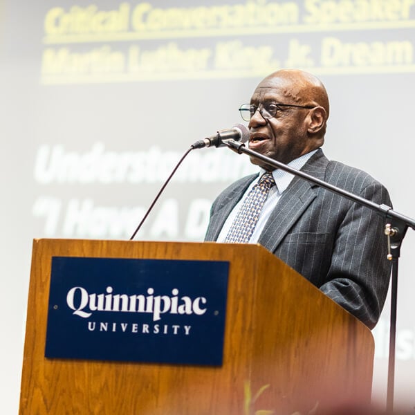 Ronald English speaks at a podium that reads Quinnipiac University