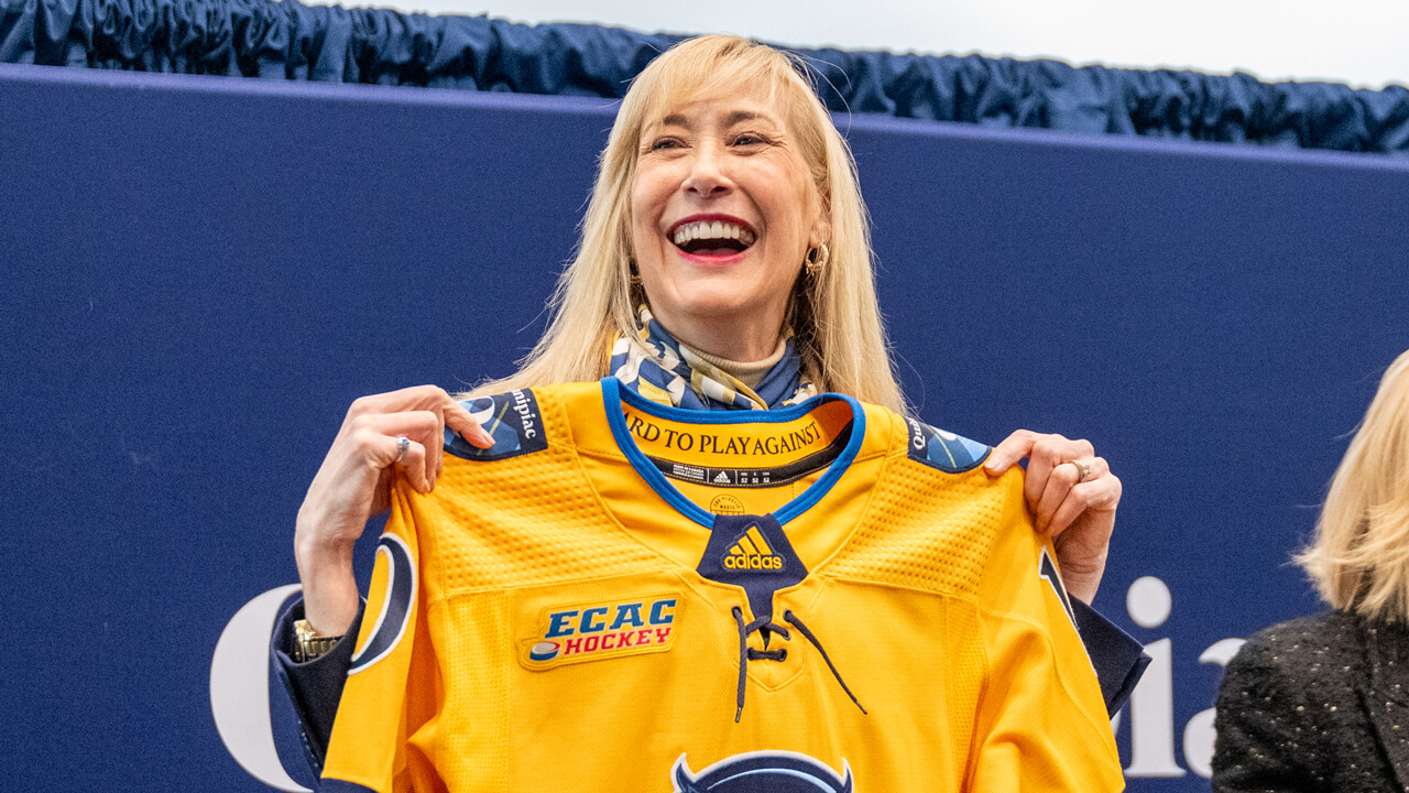 Marie Hardin smiles broadly as she holds up her new Quinnipiac women's ice hockey jersey