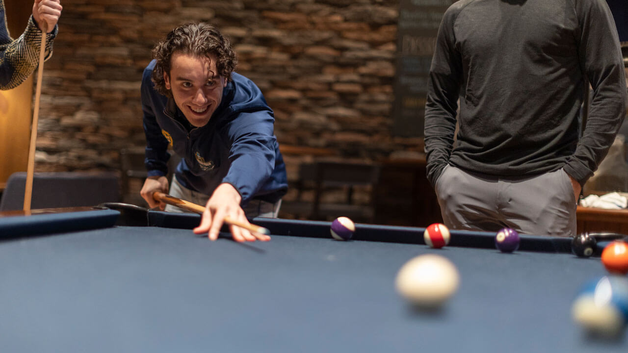 A student shoots a pool ball with a stick.