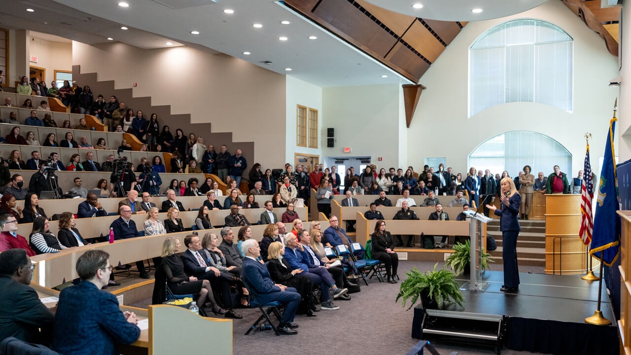 An audience packs the auditorium while Marie Hardin speaks on stage