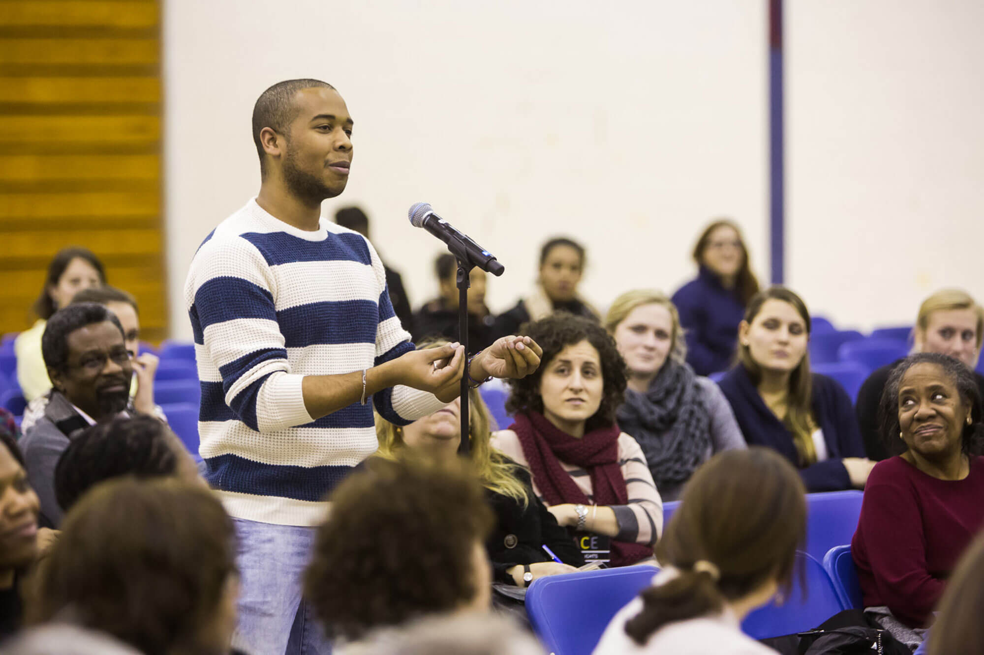 A person in the audience poses a question to Michele Norris while the audience looks on.