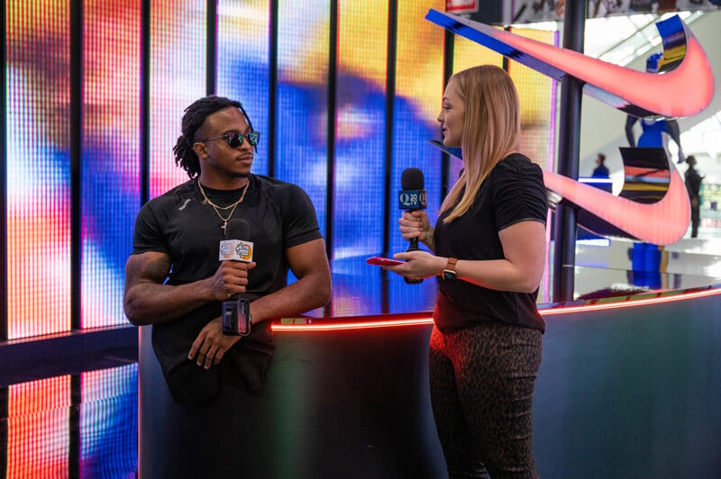 Lo Yarnall interviews Zion Clark in front of a colorfully lit wall