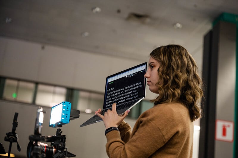 Sydney Handler holds up a computer with teleprompter words in front of a camera