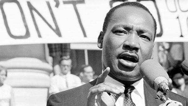 Martin Luther King Jr delivers a speech with protest signs behind him