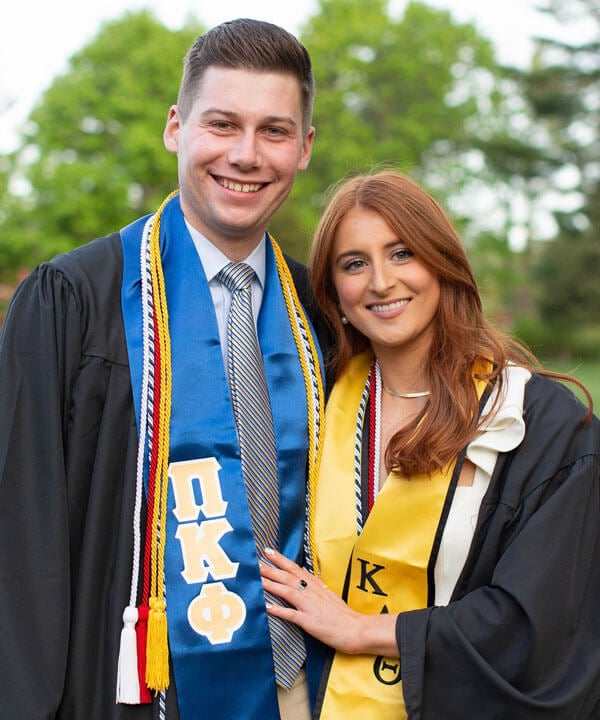 Olivia Schueller and Chris Dacey smiling in their sorority and fraternity stoles at graduation