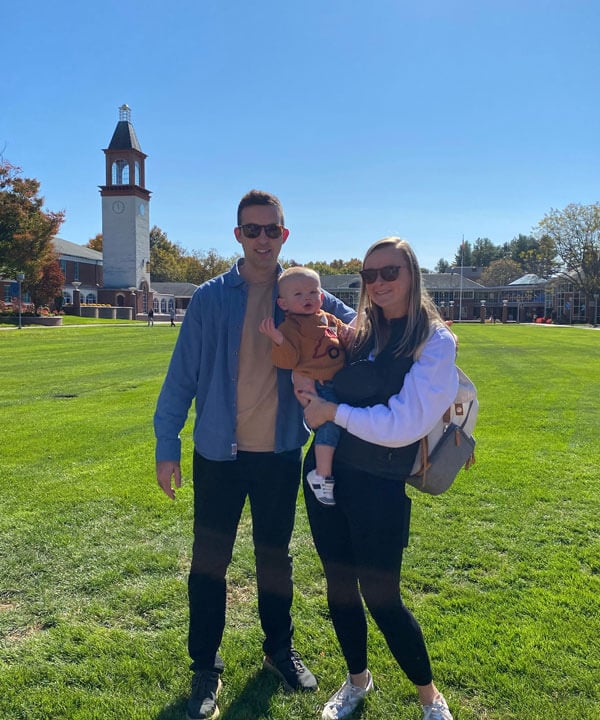 Bridget and Miles Adrian smile on the bright quad with their young child