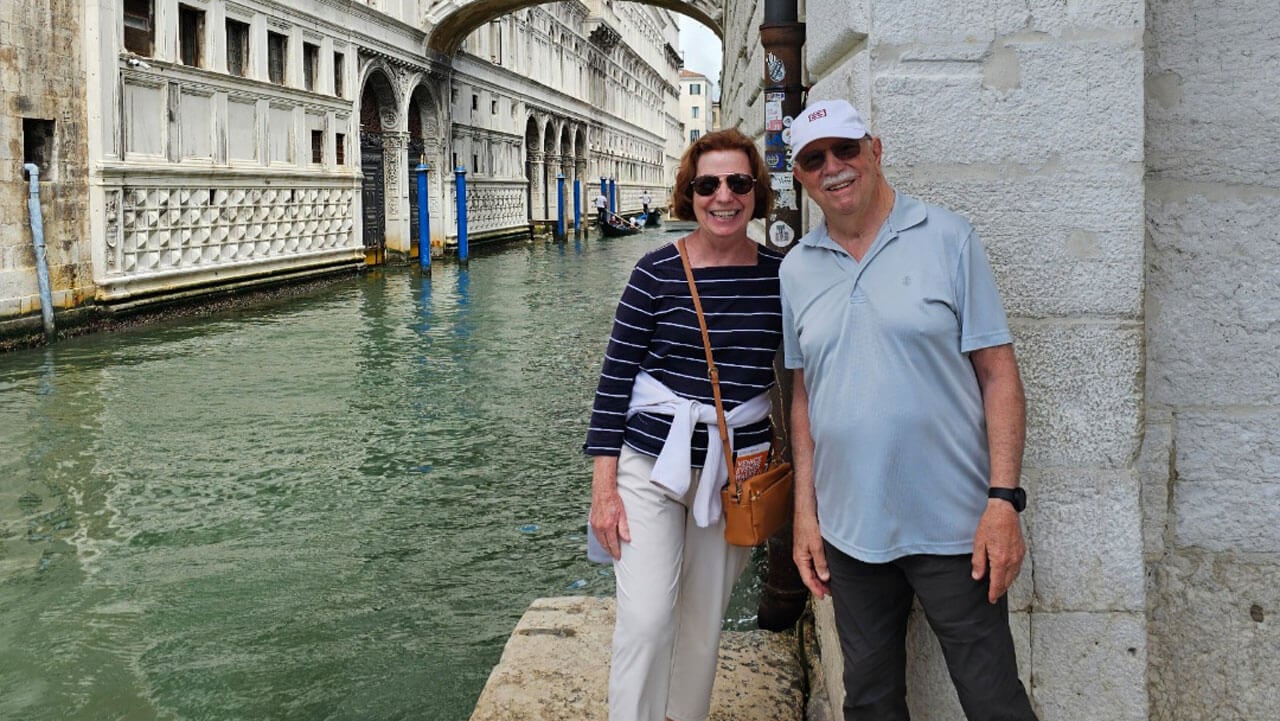 Bob and Debbie Passero smile in front of a canal on a trip