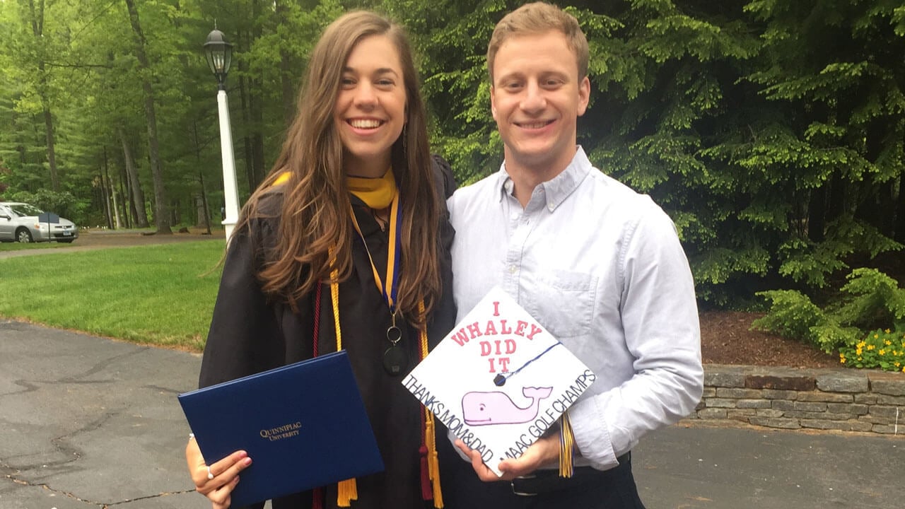 Jenn Whaley is in a graduation gown, standing next to Matt Rothbart as they both smile.