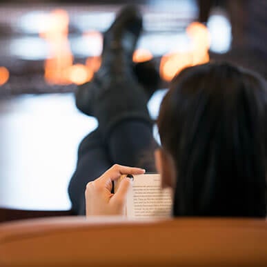 Student sits in front of fireplace with their feet up reading.