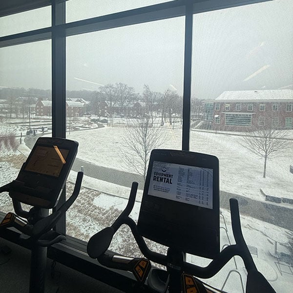 Cardio machines are shown in front of a window looking outside at snow.