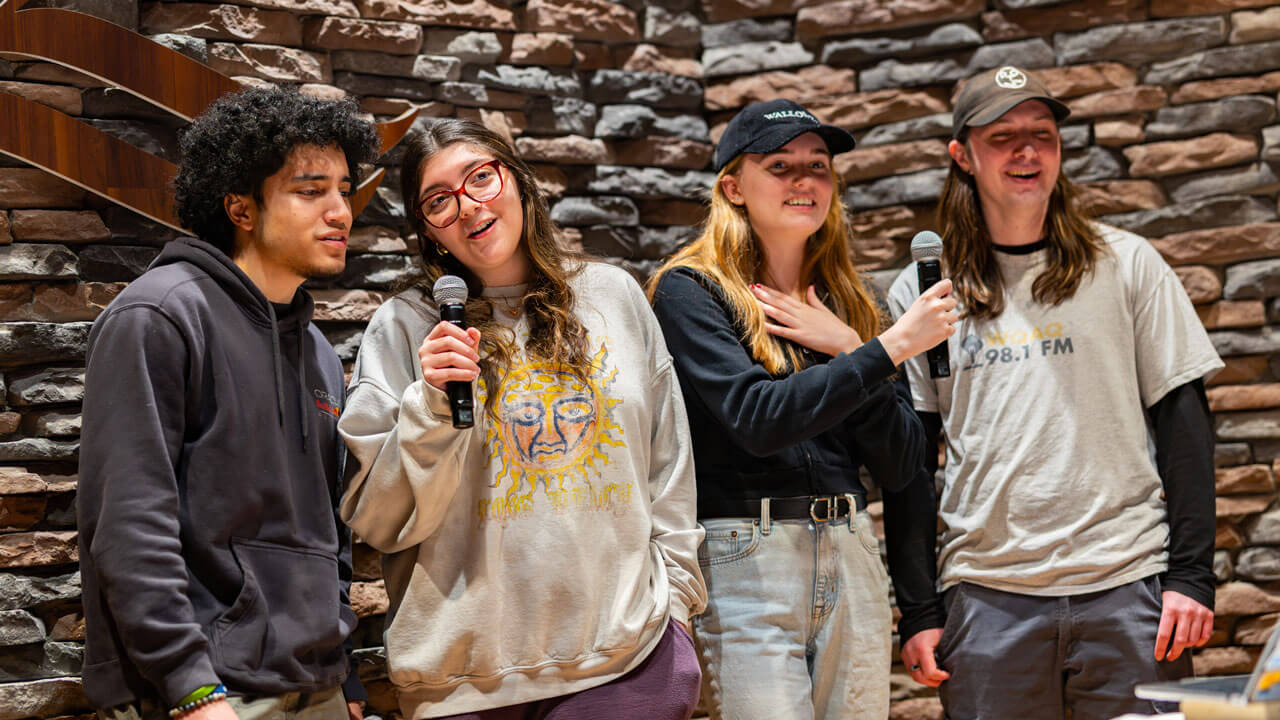 Four students hold microphones and sing together at On The Rocks