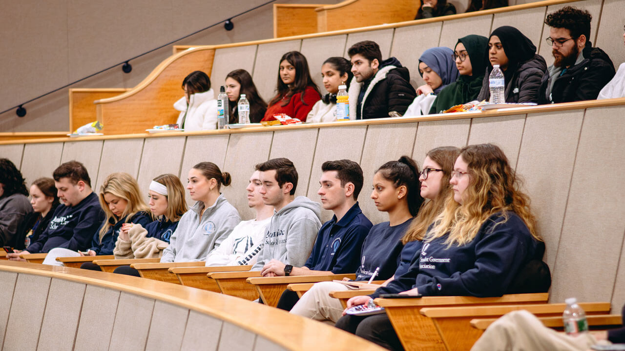 A large group of students sit in the Mount Carmel auditorium listening to speakers.