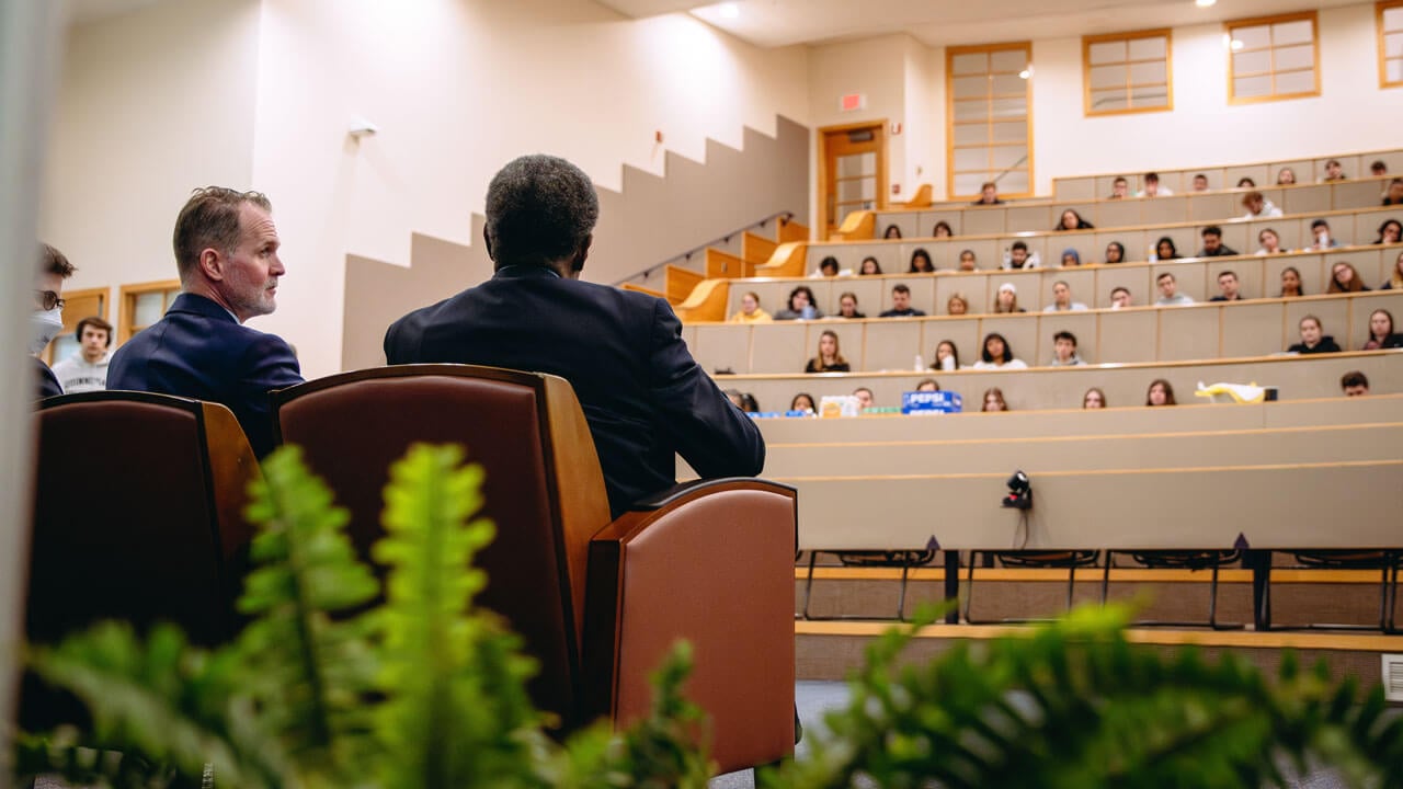 Taken from behind Tom Ellett and David Fryson, a view of the entire auditorium and students sitting. and