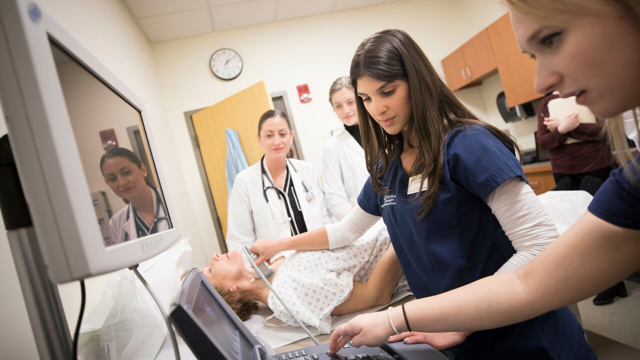 2 female students conducting an ultrasound on another female's throat with 2 other observing