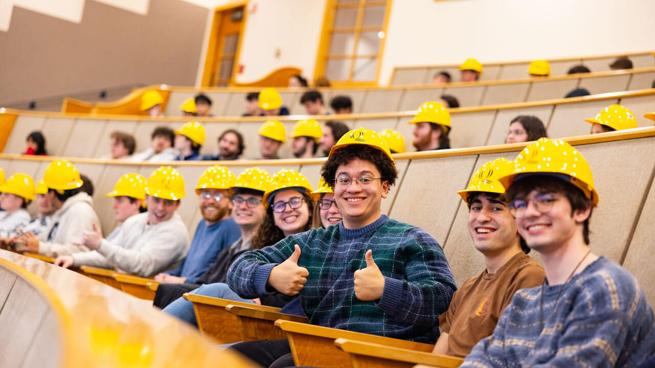 Students sit in bleachers with hard hats