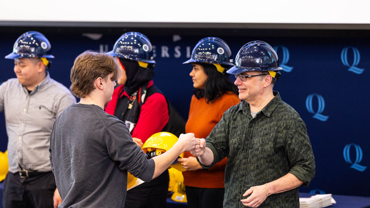 Students shake hands while receiving hard hat