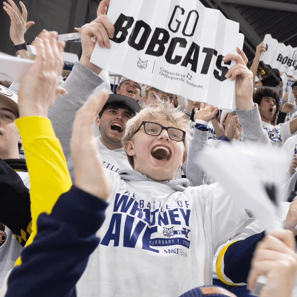 A student cheers and holds up a Go Bobcats sign in the ice hockey stands
