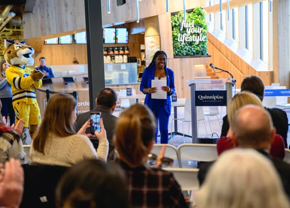 A woman stands in front of a clapping crowd while smiling