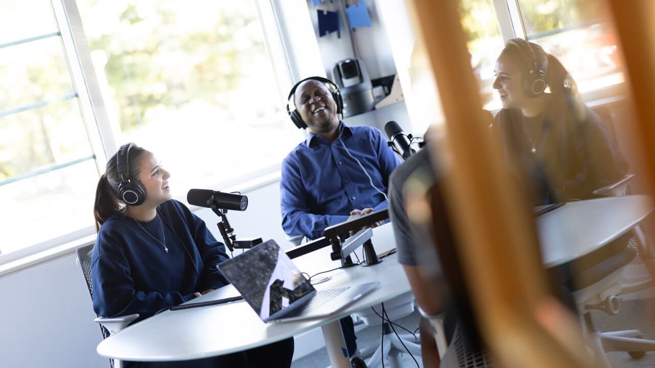 A student and faculty member converse wearing headphones in the Quinnipiac podcast studio.