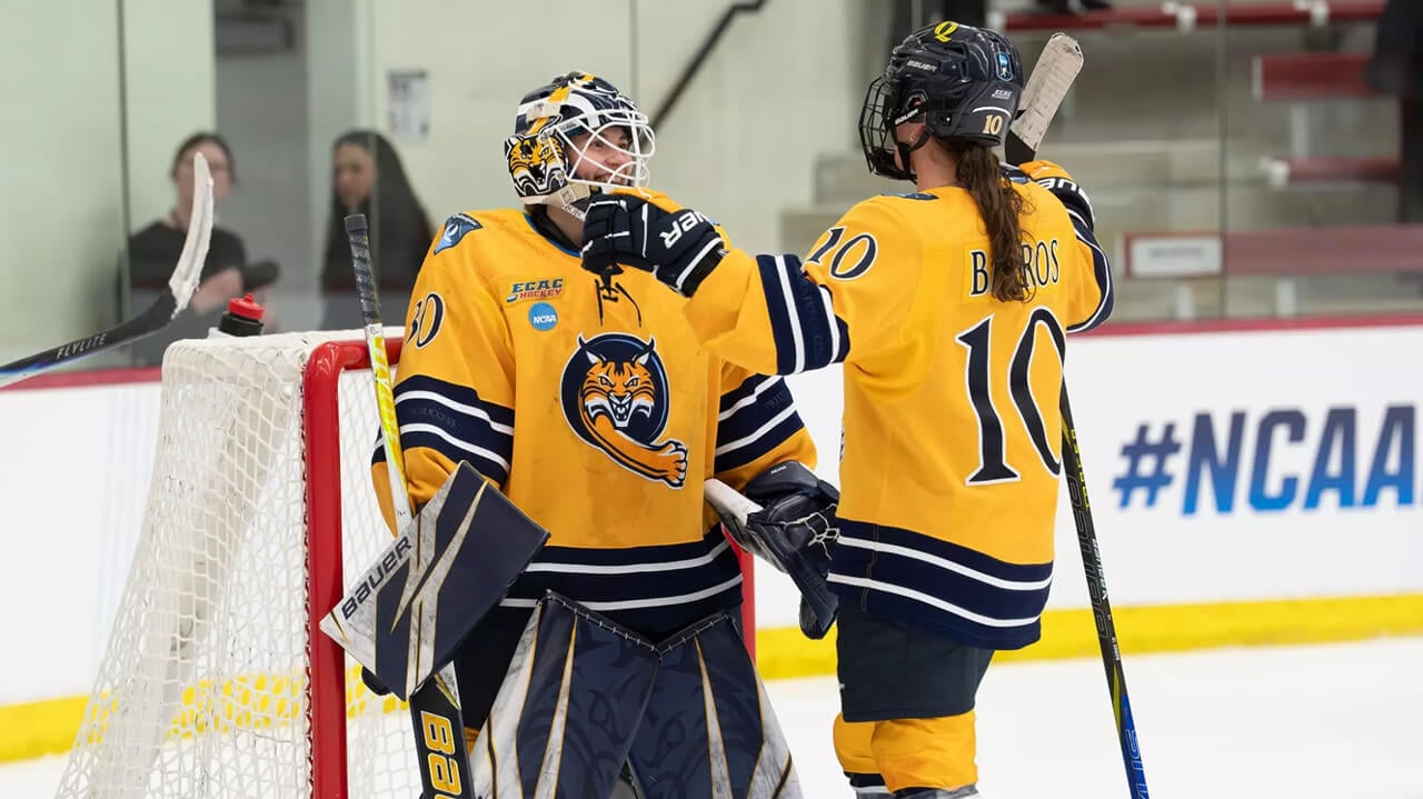 Two women's ice hockey players cheer on the ice together near the goal