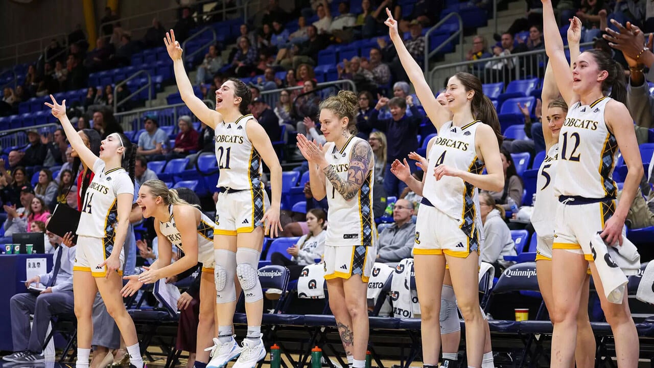 Basketball players celebrate on the sidelines by jumping.