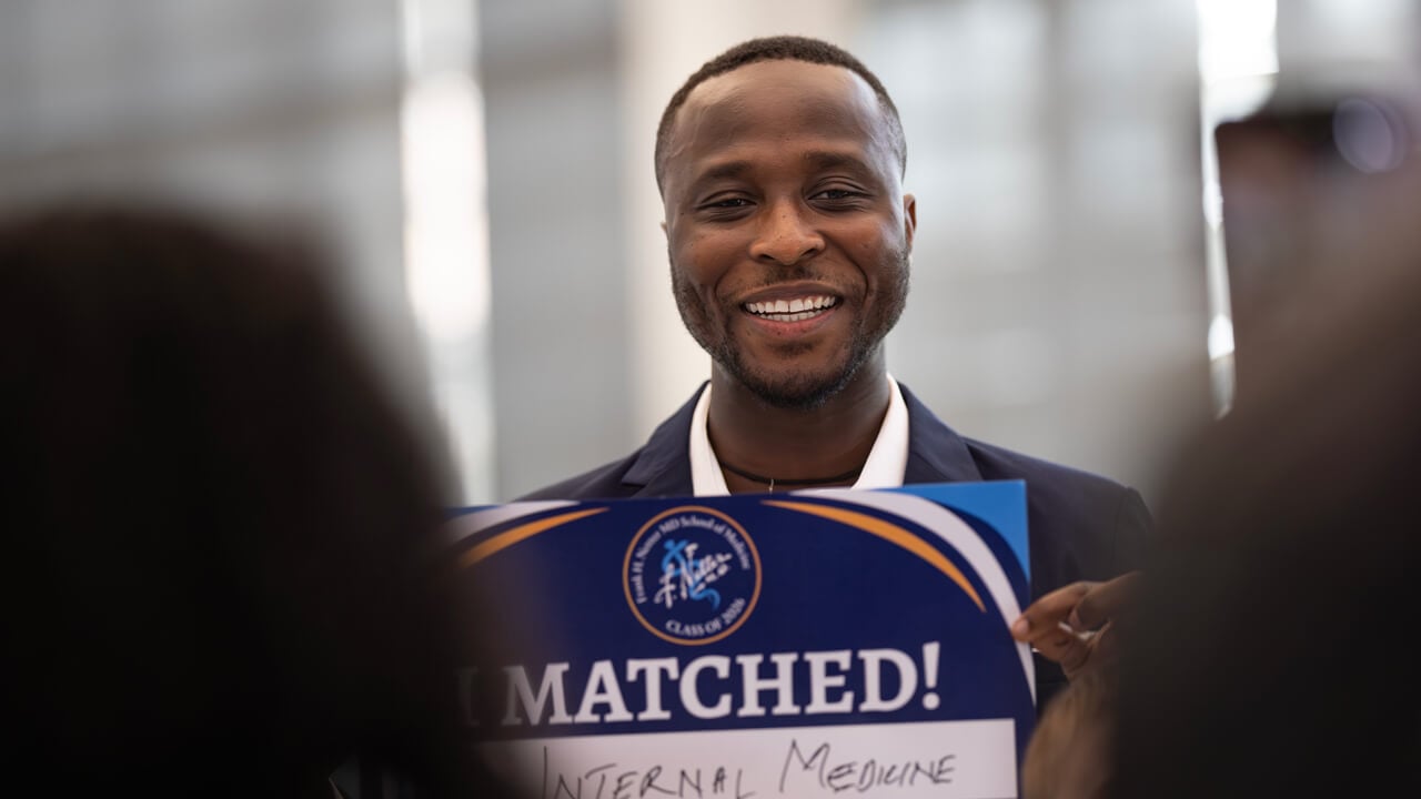 Enock Arthur smiles broadly as he holds up his "I Matched" sign