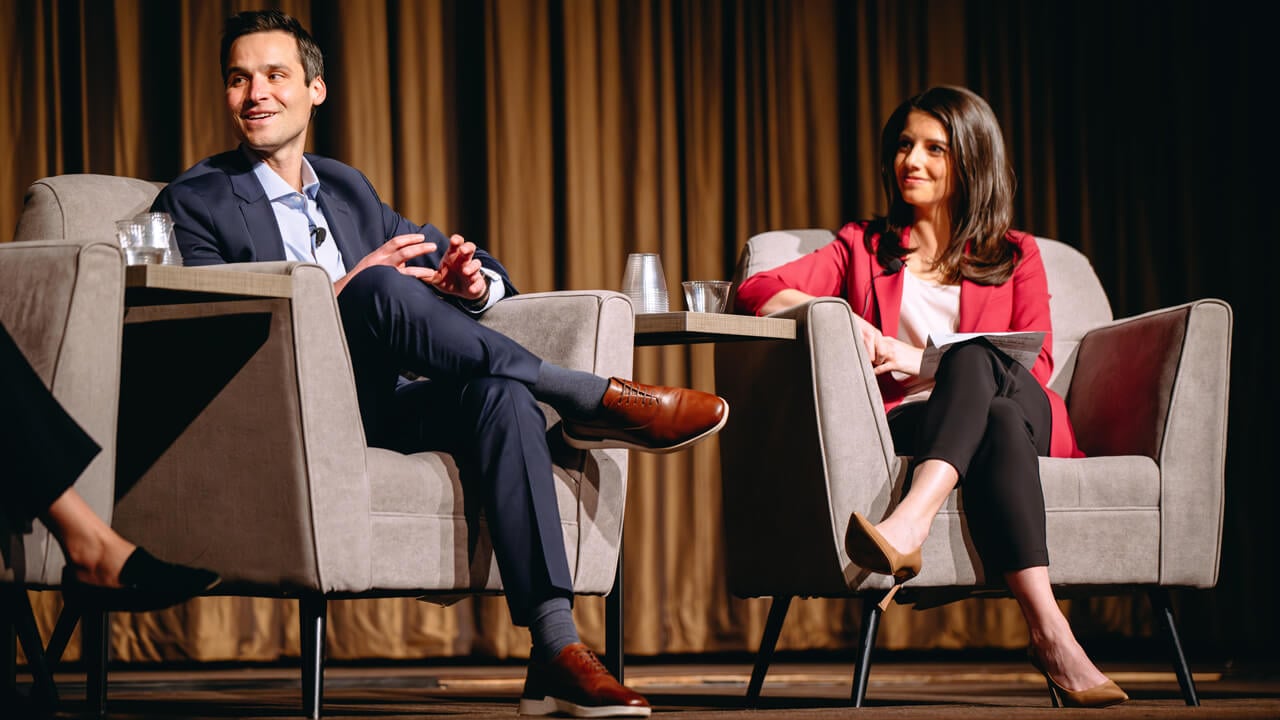 Two finance professionals sitting and talking in chair on GAME Forum stage.