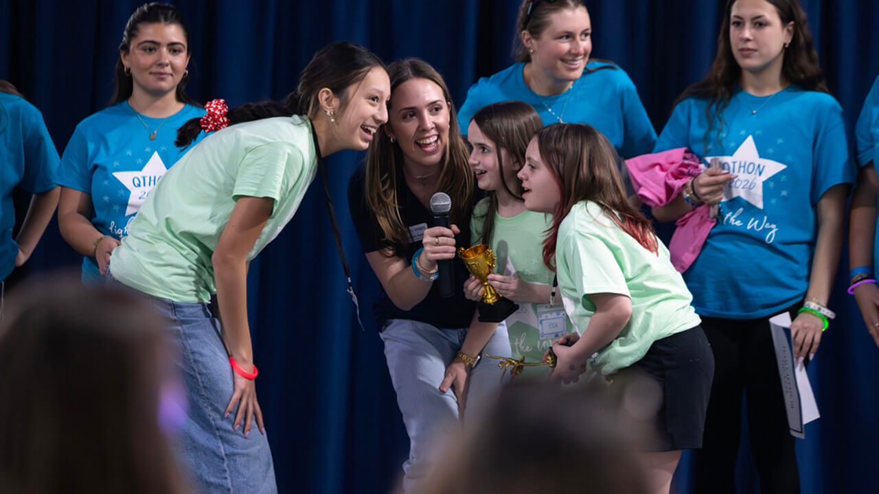 Students and miracle children stand together speaking into the microphone