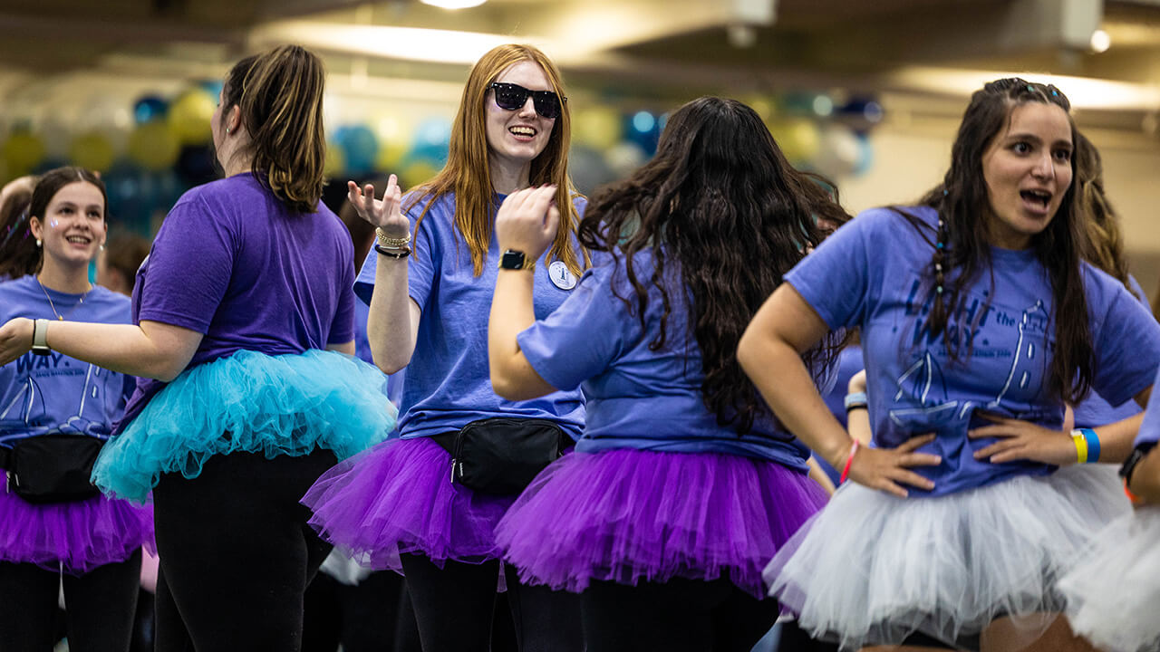 Student organization members dance together wearing tutus and QTHON gear
