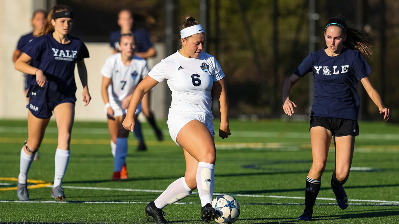 Woman running down field with opposing team chasing her