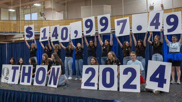 Quinnipiac students hold up signs that read $140,997.49 QTHON 2024 on stage